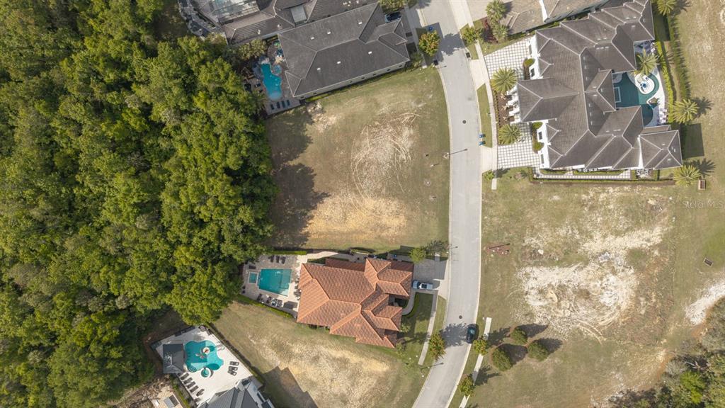 An aerial view shows a vacant residential lot situated between two large houses and woods — 8188 VALHALLA TERRACE, REUNION, FL
