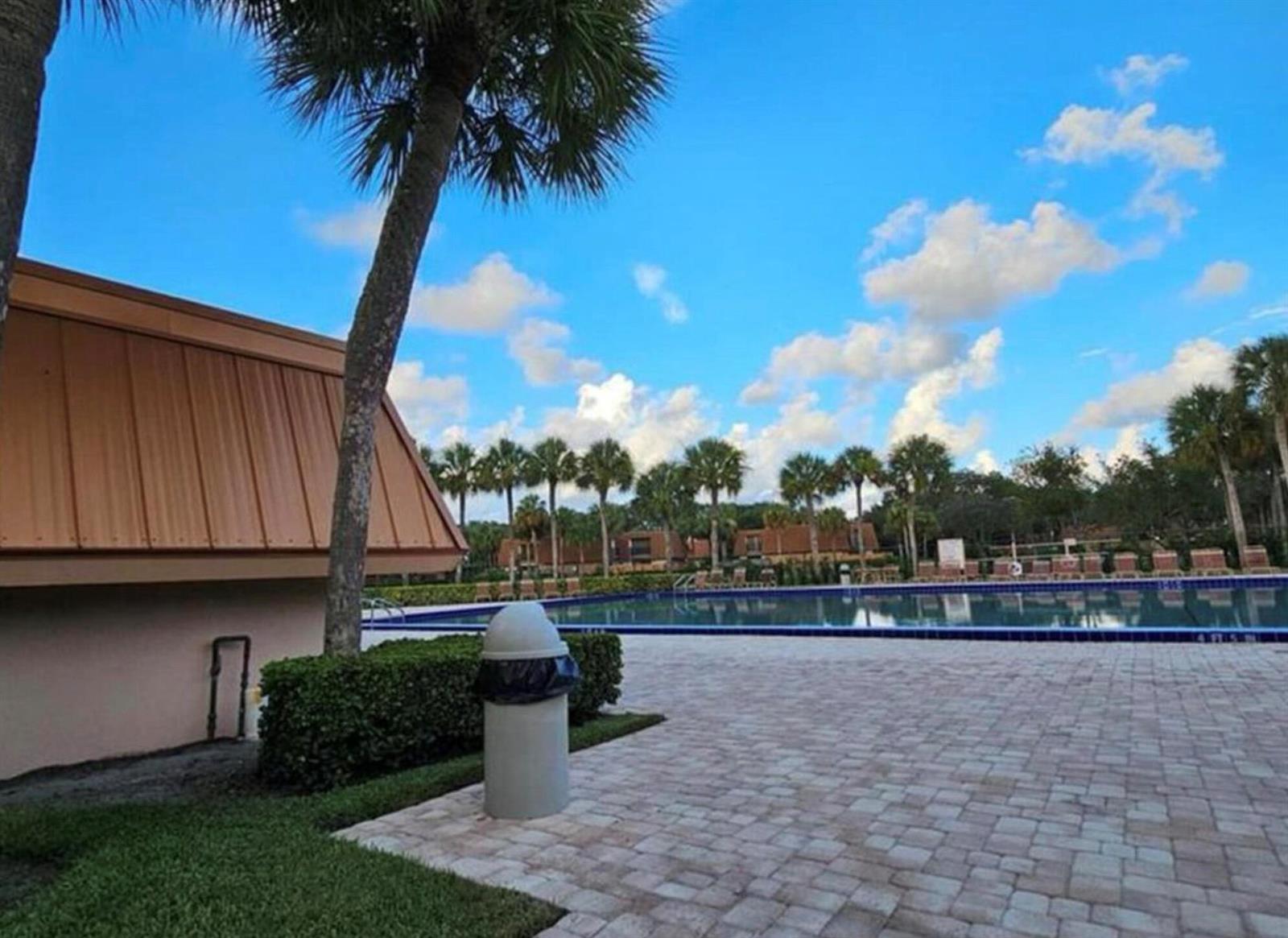 A paved pool deck features a trash receptacle, a palm tree, and a swimming pool — 197 Charter Way, West Palm Beach FL 33407, WEST PALM BEACH, FL