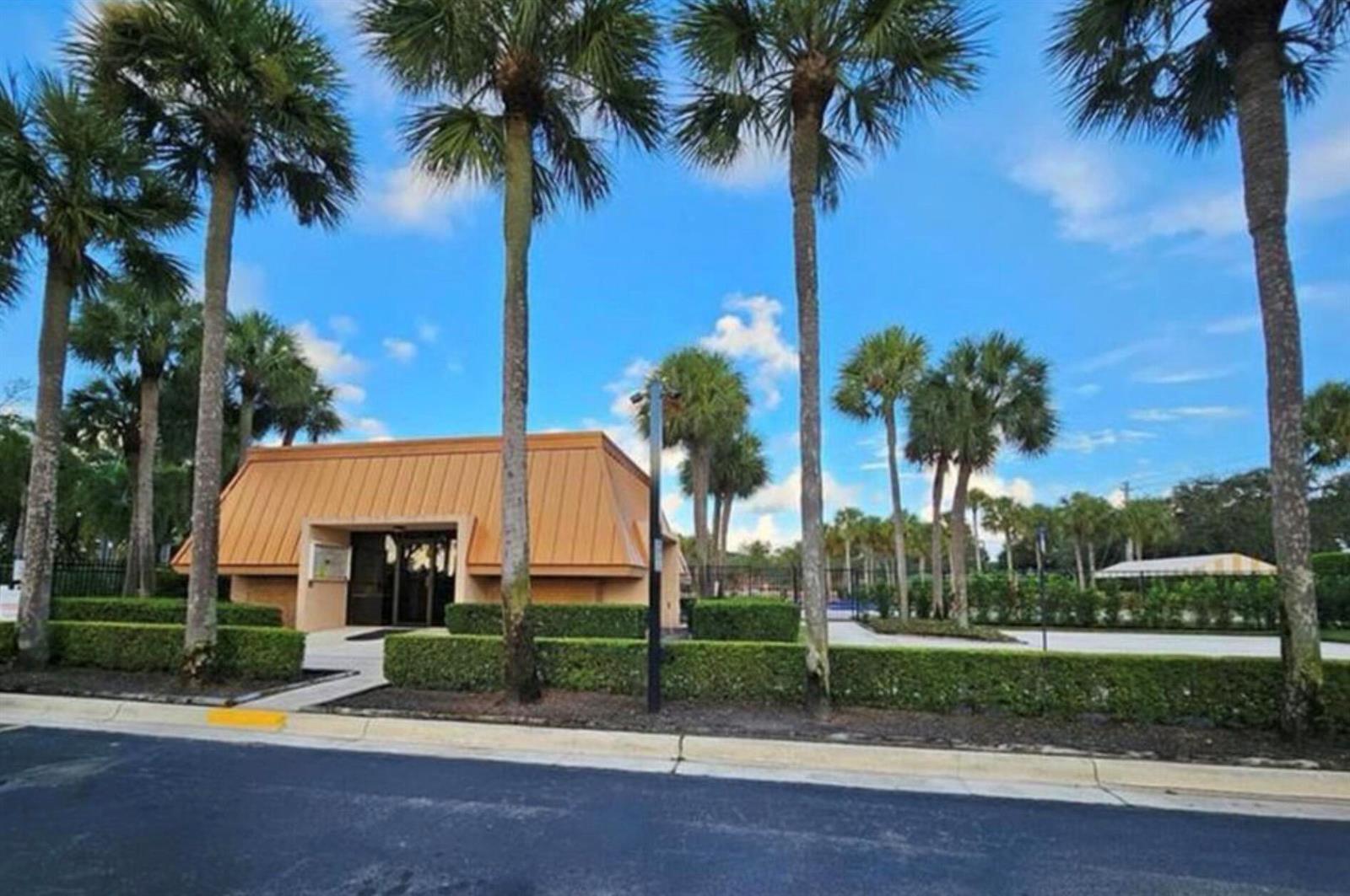 A tan building with a sloped roof stands behind manicured hedges and tall palm trees — 197 Charter Way, West Palm Beach FL 33407, WEST PALM BEACH, FL