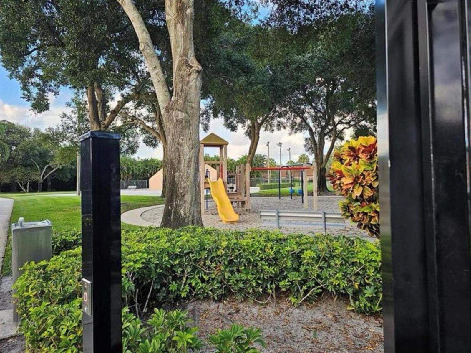 A playground with a yellow slide and swings sits in a park with large trees — 197 Charter Way, West Palm Beach FL 33407, WEST PALM BEACH, FL