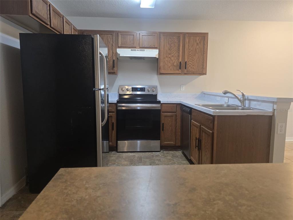 A kitchen features wood cabinets, a black refrigerator, a stainless steel stove, and laminate countertops — 219 GLOWING PEACE LN UNIT 85, ORLANDO, FL