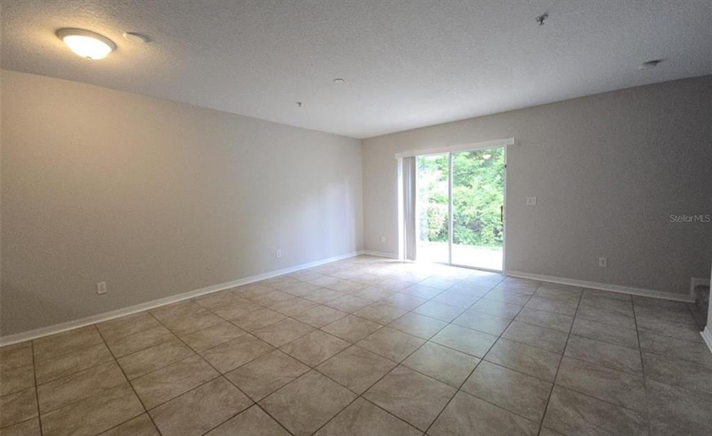 An empty living room features beige walls, light-colored tile flooring, and a sliding glass door — 219 GLOWING PEACE LN UNIT 85, ORLANDO, FL