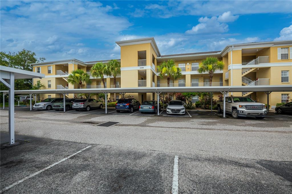 A three-story yellow apartment building with covered parking spaces in the foreground — 19355 WATER OAK DRIVE UNIT 101, PORT CHARLOTTE, FL