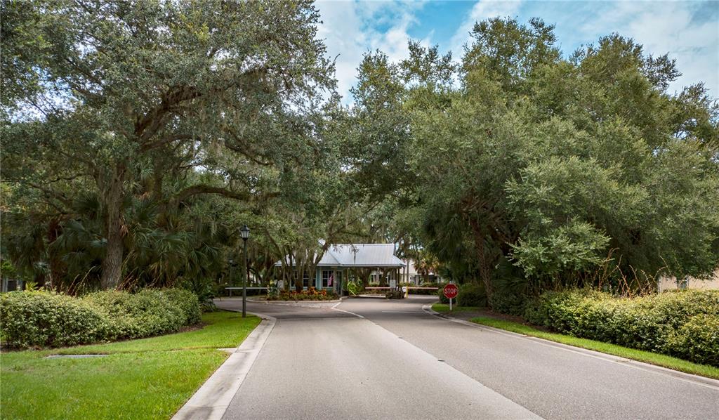 A paved road leads to a gated community entrance shaded by large, moss-draped oak trees — 19355 WATER OAK DRIVE UNIT 101, PORT CHARLOTTE, FL