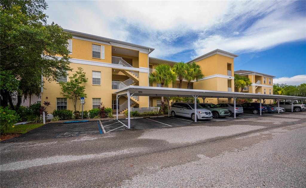 A three-story yellow apartment building features a covered parking structure in the foreground — 19355 WATER OAK DRIVE UNIT 101, PORT CHARLOTTE, FL