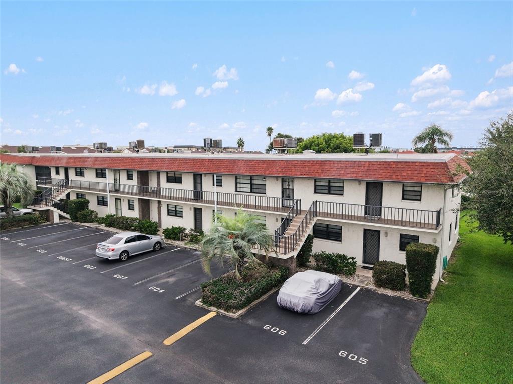 An exterior view of a two-story apartment building with a red shingled roof and parking — 200 SAINT LUCIE LANE UNIT 605, COCOA BEACH, FL