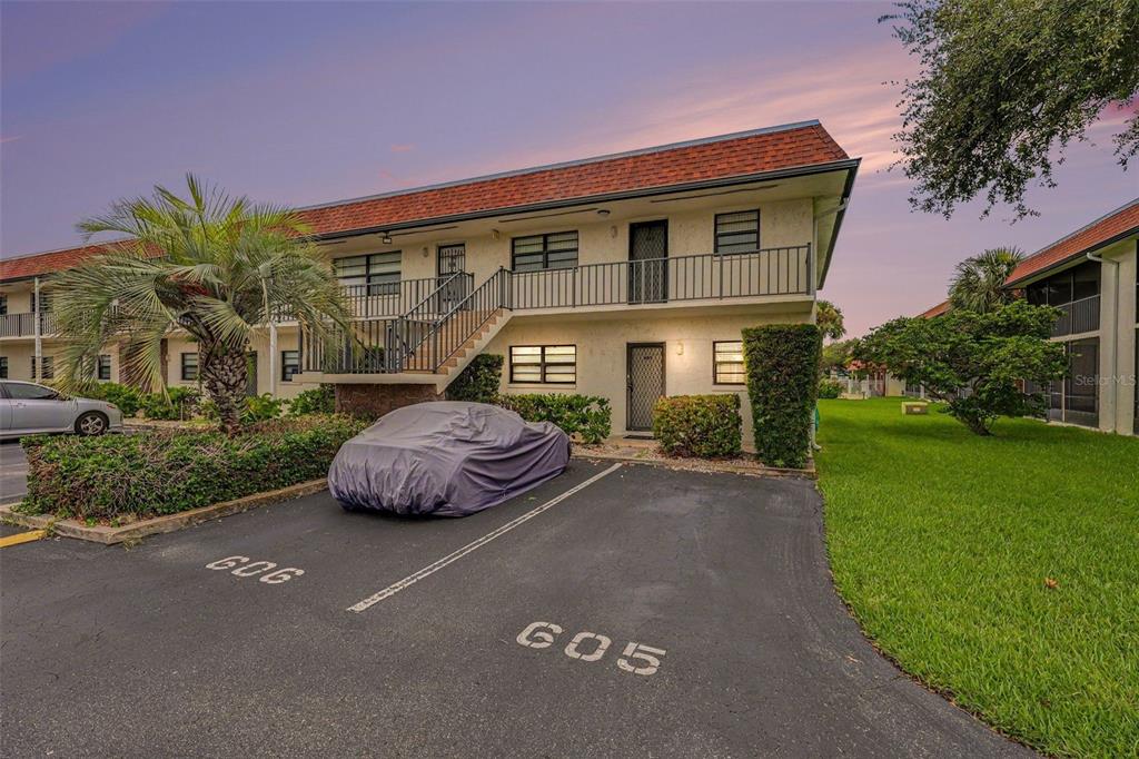 A two-story apartment building exterior features a covered car, parking spaces, and a staircase — 200 SAINT LUCIE LANE UNIT 605, COCOA BEACH, FL