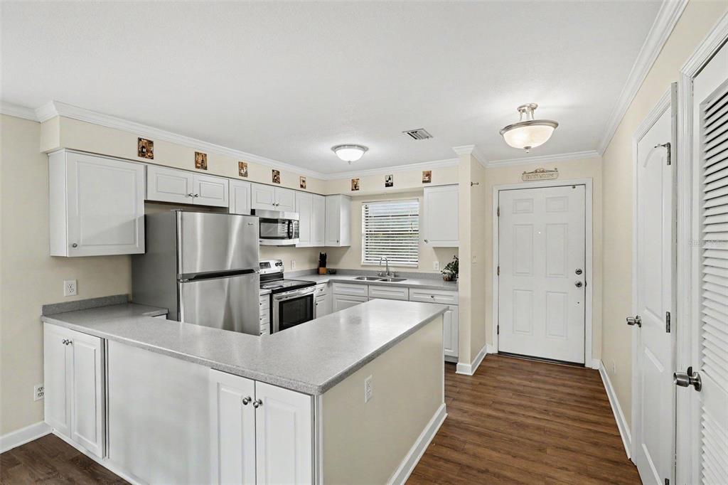 A kitchen features white cabinets, stainless steel appliances, gray countertops, and wood-look flooring — 200 SAINT LUCIE LANE UNIT 605, COCOA BEACH, FL