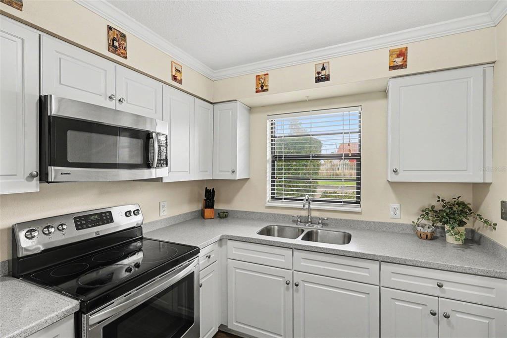 A kitchen with white cabinets, stainless steel appliances, gray countertops, and a window above the sink — 200 SAINT LUCIE LANE UNIT 605, COCOA BEACH, FL