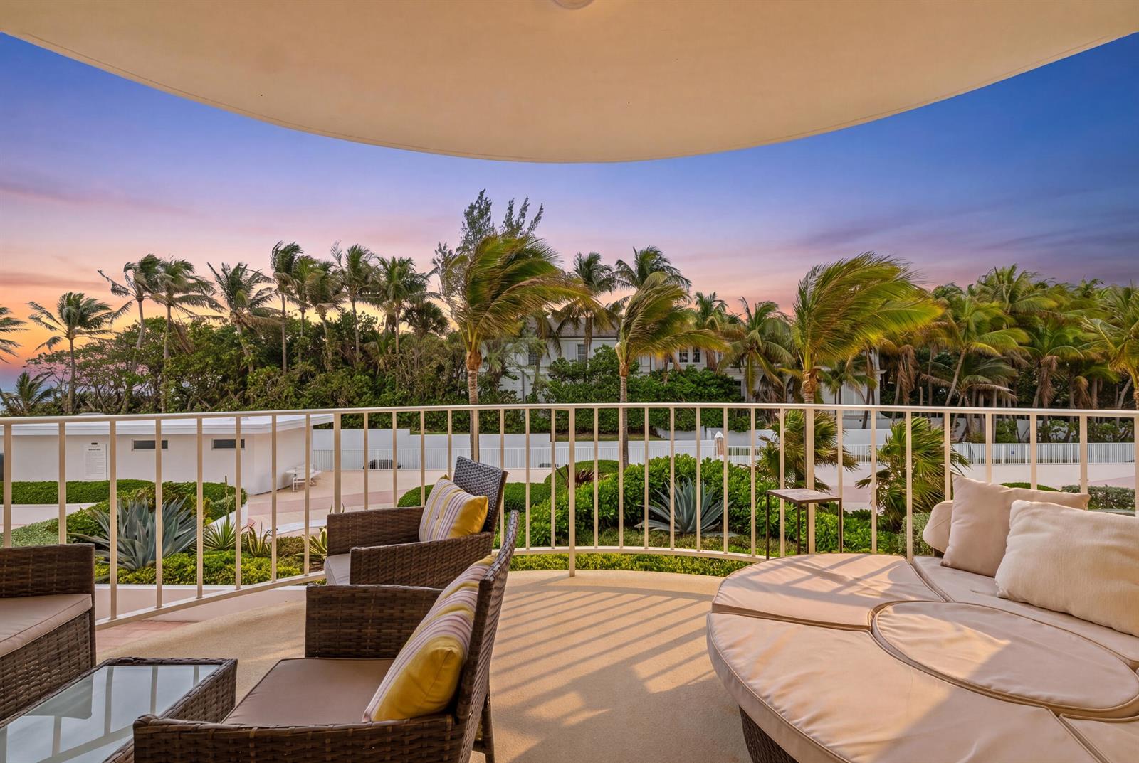 A balcony with wicker chairs and a circular daybed overlooks palm trees at sunset — 2295 S Ocean Boulevard # 302, Palm Beach FL 33480, PALM BEACH, FL