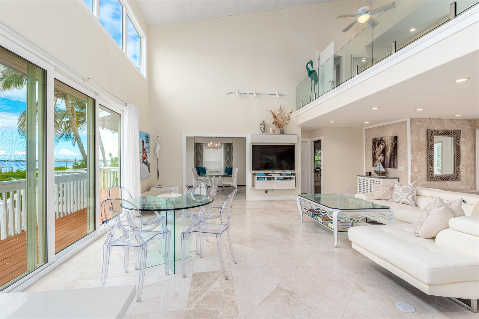 A bright, open-concept living and dining area features high ceilings, tile floors, and glass furniture — 1470 SE Macarthur Boulevard, Stuart FL 34996, STUART, FL