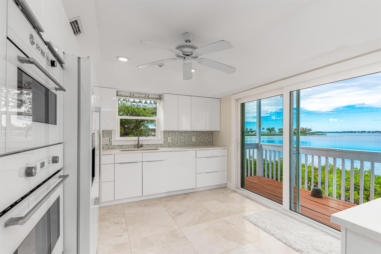 A white kitchen with modern cabinets, a ceiling fan, and sliding doors overlooking the water — 1470 SE Macarthur Boulevard, Stuart FL 34996, STUART, FL