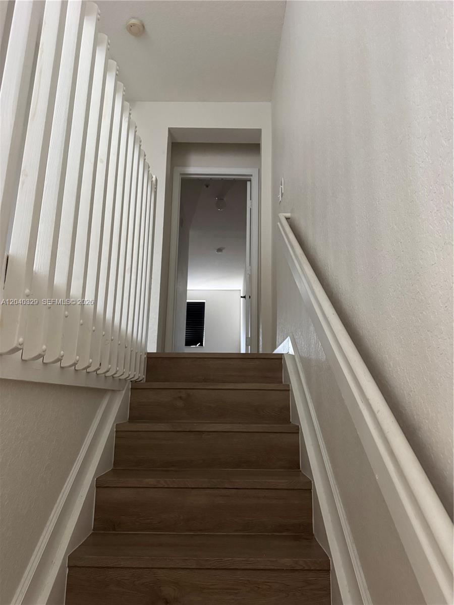 A staircase with wood-look treads leads to an open doorway in a white hallway — 17640 NW 73rd Ave # 19, Hialeah FL 33015, HIALEAH, FL