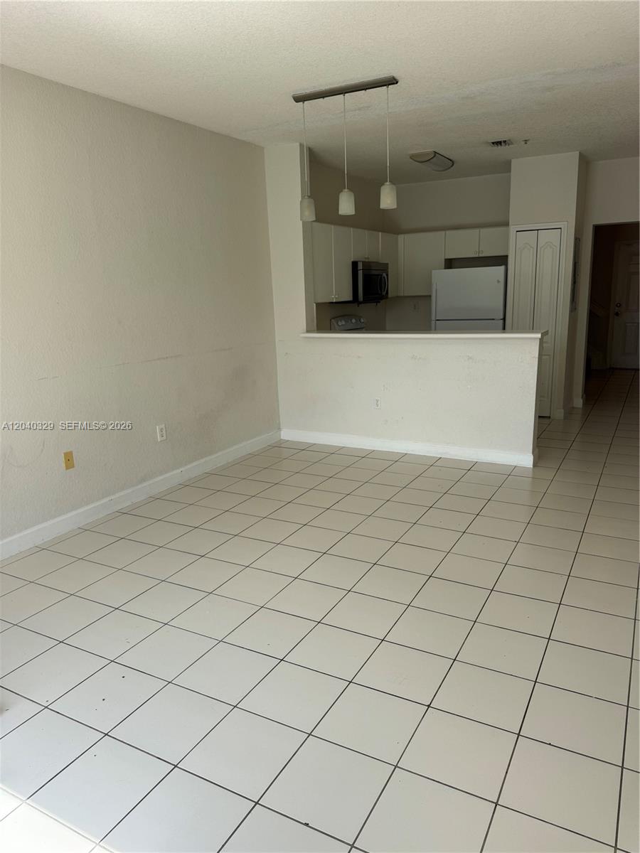 This room features white tile flooring, a kitchen pass-through counter, and three pendant lights — 17640 NW 73rd Ave # 19, Hialeah FL 33015, HIALEAH, FL