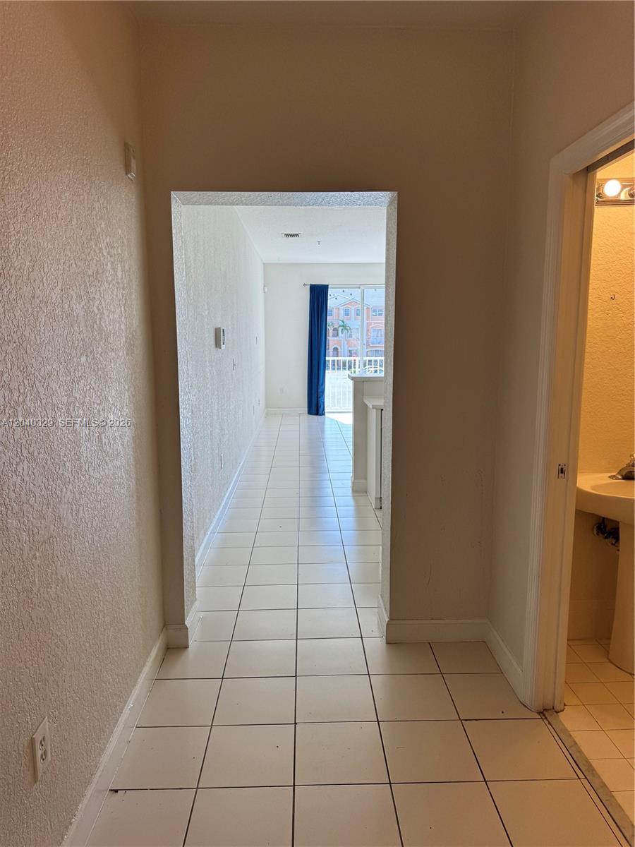 A tiled hallway leads to a living area with a balcony and blue curtains — 17640 NW 73rd Ave # 19, Hialeah FL 33015, HIALEAH, FL