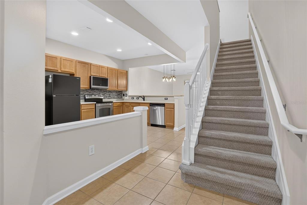 A kitchen with wood cabinets and stainless appliances sits beside a carpeted staircase — 10137 PINK PALMATA COURT, RIVERVIEW, FL