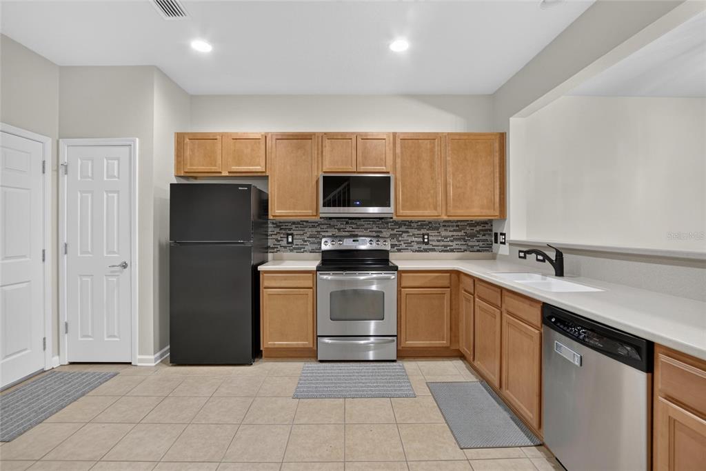A kitchen features light wood cabinets, stainless steel appliances, a black refrigerator, and tile flooring — 10137 PINK PALMATA COURT, RIVERVIEW, FL