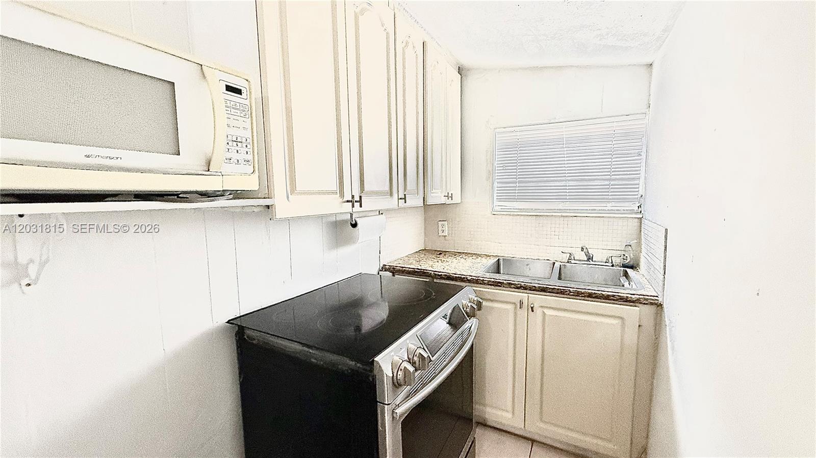 A small kitchen features white cabinets, a black electric stove, and a stainless steel sink — 1878 NW 112th Ter # 1, Miami FL 33167, MIAMI, FL
