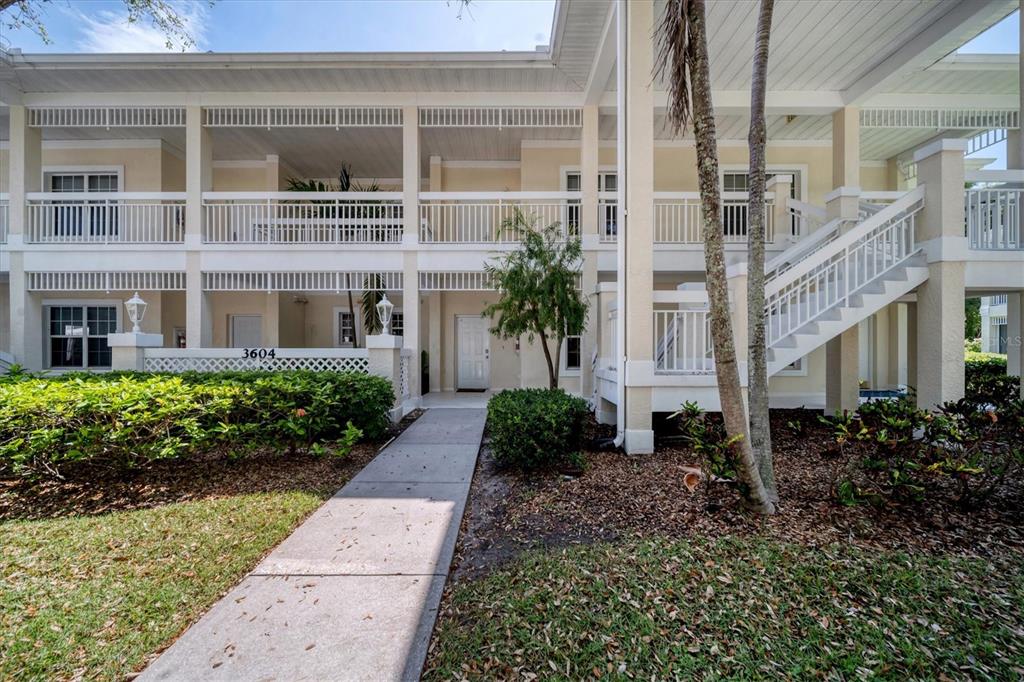 A two-story residential building features a concrete walkway leading to a ground-floor entrance — 3604 54TH DRIVE W UNIT 102, BRADENTON, FL