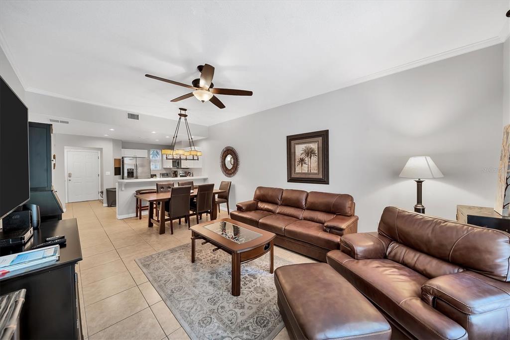 A living room and dining area with tile floors, brown leather furniture, and a ceiling fan — 3604 54TH DRIVE W UNIT 102, BRADENTON, FL