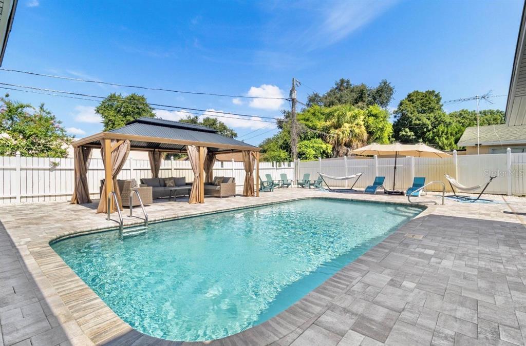 A backyard features a swimming pool, a covered gazebo with seating, and a white fence — 5127 CAESAR WAY S, ST PETERSBURG, FL