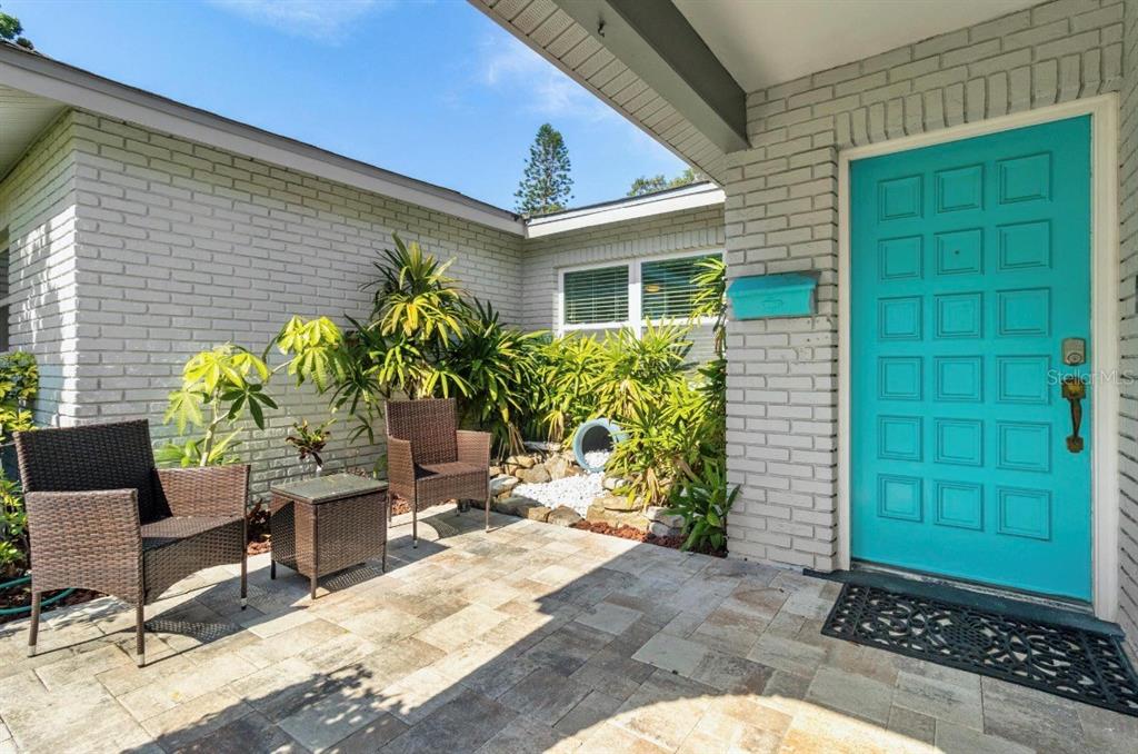 A patio with two wicker chairs and a table sits beside a bright turquoise door — 5127 CAESAR WAY S, ST PETERSBURG, FL