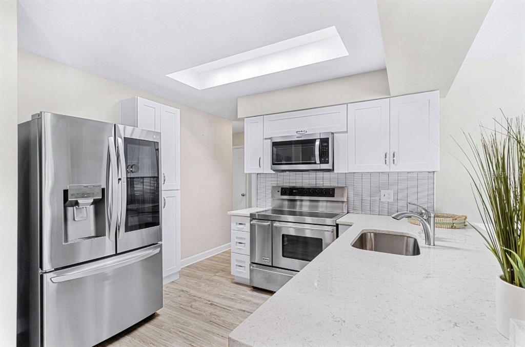 A kitchen features white cabinets, stainless steel appliances, a quartz countertop, and light wood flooring — 5127 CAESAR WAY S, ST PETERSBURG, FL
