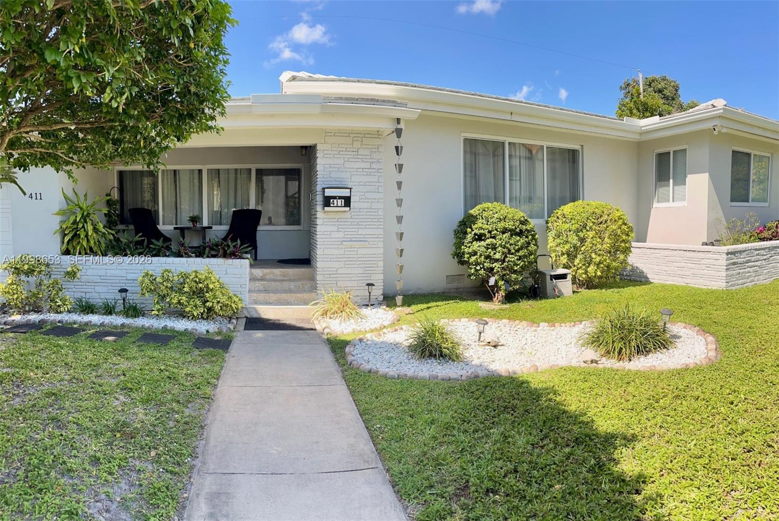 A single-story house with a white exterior, stone accents, a front porch, and landscaped yard — 411 Alesio Ave, Coral Gables FL 33134, CORAL GABLES, FL