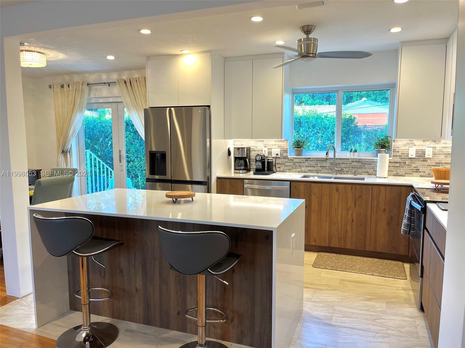 A modern kitchen features a white quartz island, wood-grain cabinetry, stainless steel appliances, and tile flooring — 411 Alesio Ave, Coral Gables FL 33134, CORAL GABLES, FL