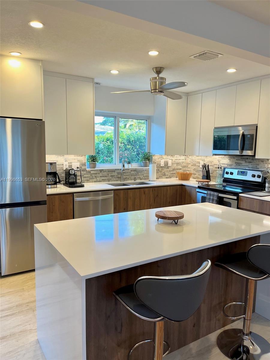 A modern kitchen features white upper cabinets, wood-tone lower cabinets, and a central island — 411 Alesio Ave, Coral Gables FL 33134, CORAL GABLES, FL