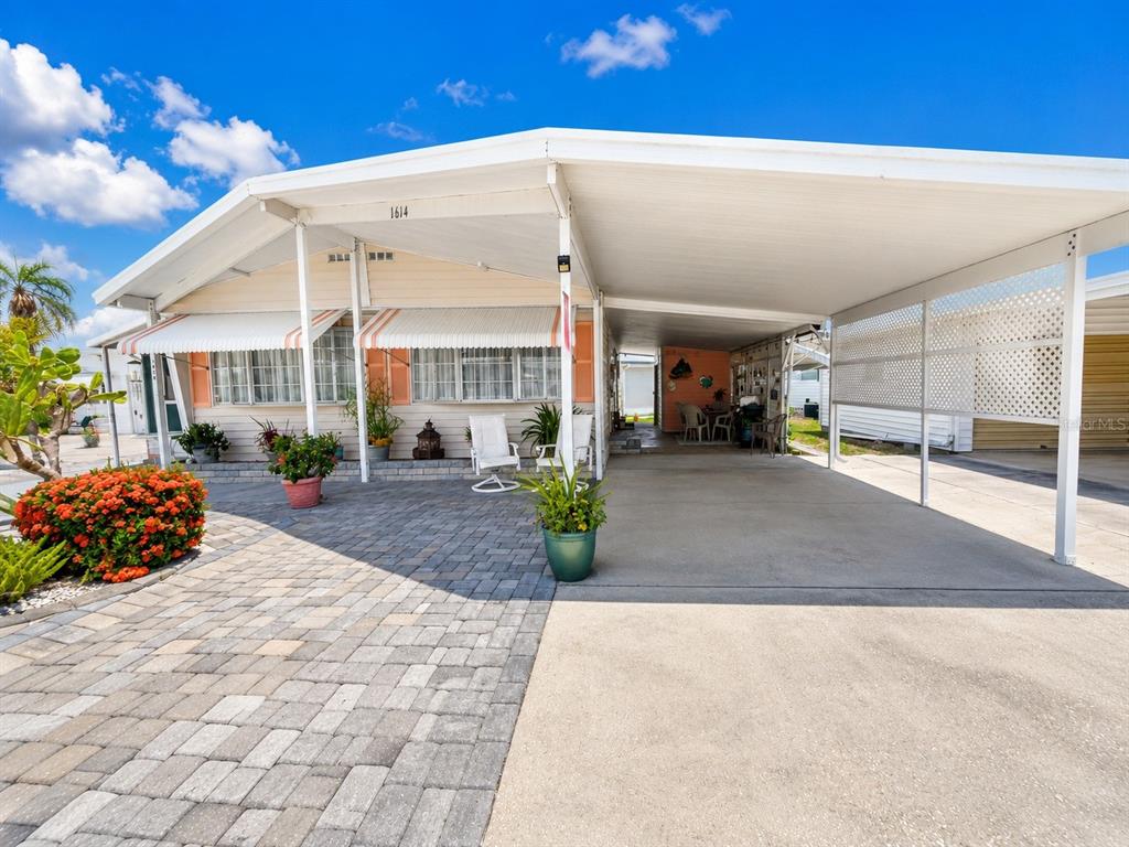 A mobile home exterior features a paved patio, a large carport, and striped window awnings — 1614 MICHIGAN AVENUE, BRADENTON, FL