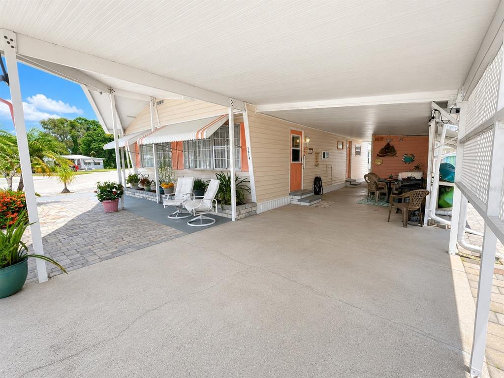A mobile home exterior features a covered carport, a paved patio, and two white chairs — 1614 MICHIGAN AVENUE, BRADENTON, FL