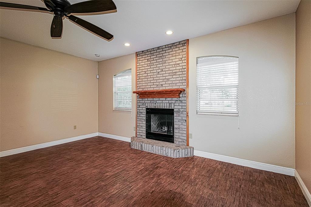 A living room features wood-look flooring, a brick fireplace, and a ceiling fan — 13768 RUDI LOOP, SPRING HILL, FL