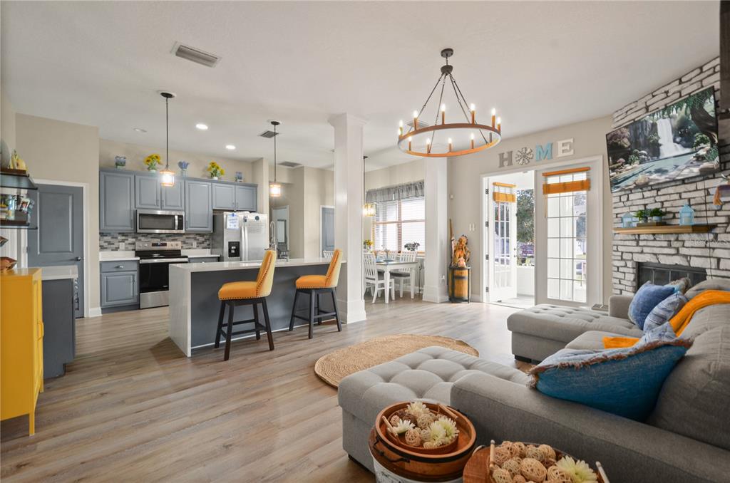 An open-concept living room and kitchen featuring gray cabinetry, a stone fireplace, and wood flooring — 331 EASTERN AVENUE, ST CLOUD, FL