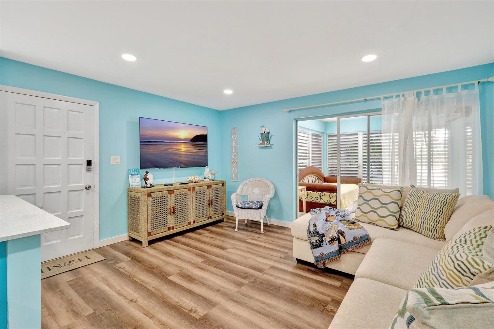 A living room features light blue walls, wood-look flooring, a television, and a sectional sofa — 11000 S Ocean Drive # 1d, Jensen Beach FL 34957, JENSEN BEACH, FL