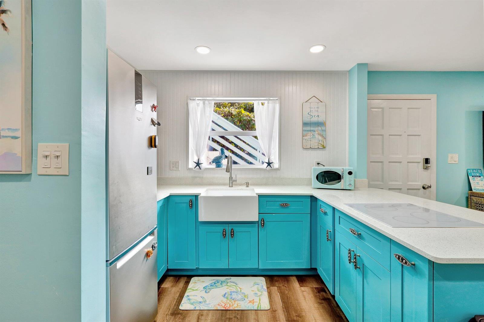 A kitchen features bright turquoise cabinets, a white farmhouse sink, and a stainless steel refrigerator — 11000 S Ocean Drive # 1d, Jensen Beach FL 34957, JENSEN BEACH, FL