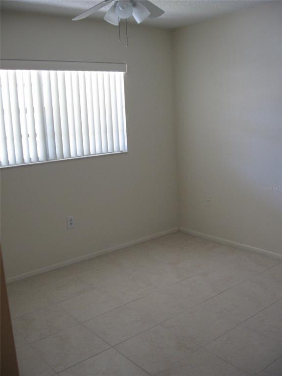 An empty bedroom features light-colored tile flooring, off-white walls, and a window with vertical blinds — 2465 NORTHSIDE DRIVE UNIT 603, CLEARWATER, FL