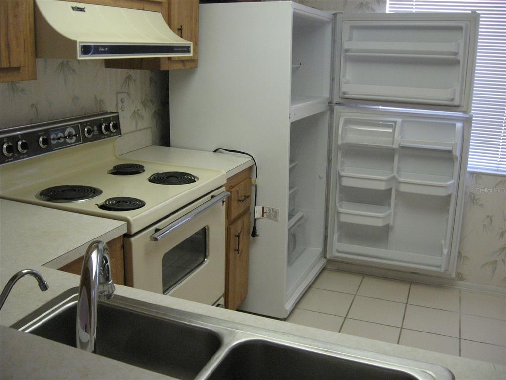A kitchen features a white stove, an open refrigerator, and a double-basin stainless steel sink — 2465 NORTHSIDE DRIVE UNIT 603, CLEARWATER, FL