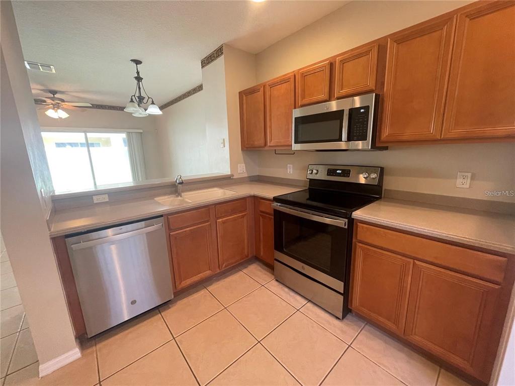 A kitchen features wood cabinets, stainless steel appliances, and tile flooring — 8508 BRUSHLEAF WAY, TAMPA, FL