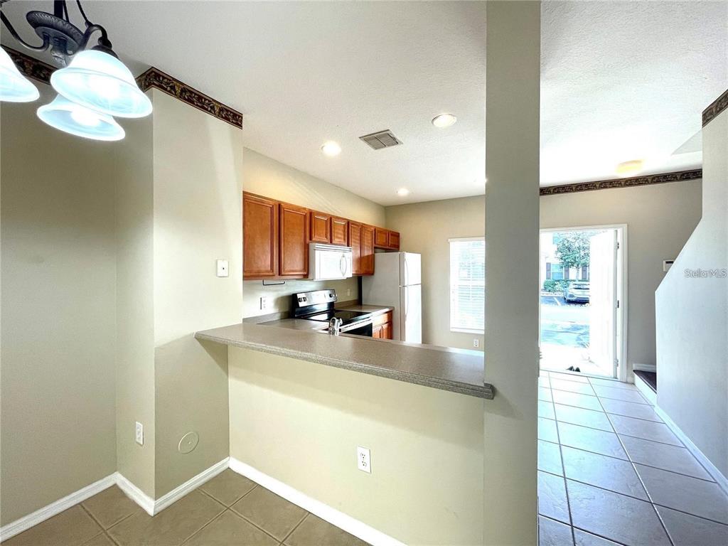 A kitchen with wood cabinets, white appliances, and a breakfast bar overlooks a tiled entryway — 8508 BRUSHLEAF WAY, TAMPA, FL
