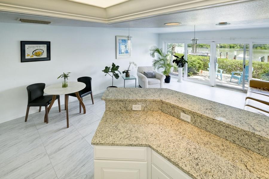 A kitchen with granite countertops overlooks a dining area and a patio with water views — 6700 GULF OF MEXICO DRIVE UNIT 118, LONGBOAT KEY, FL
