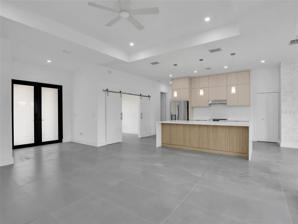 A modern kitchen with light wood cabinets and a large island overlooks an open living area — 11153 CARNEGIE AVENUE, ENGLEWOOD, FL