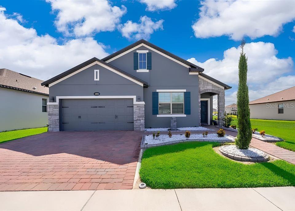 A single-story house with a gray exterior, stone accents, and a paved driveway — 1881 NAPOLI DRIVE, ST CLOUD, FL
