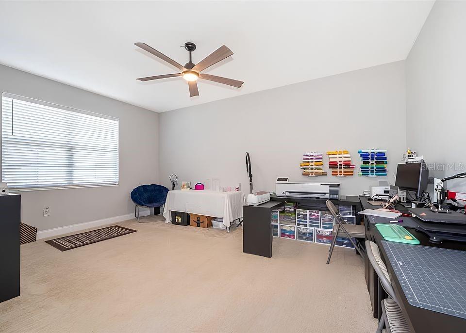 A craft room features a ceiling fan, carpeted flooring, and multiple desks with organized supplies — 1881 NAPOLI DRIVE, ST CLOUD, FL