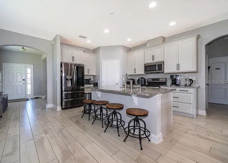 A kitchen with light gray cabinets, granite countertops, a central island, and wood-look tile flooring — 1881 NAPOLI DRIVE, ST CLOUD, FL
