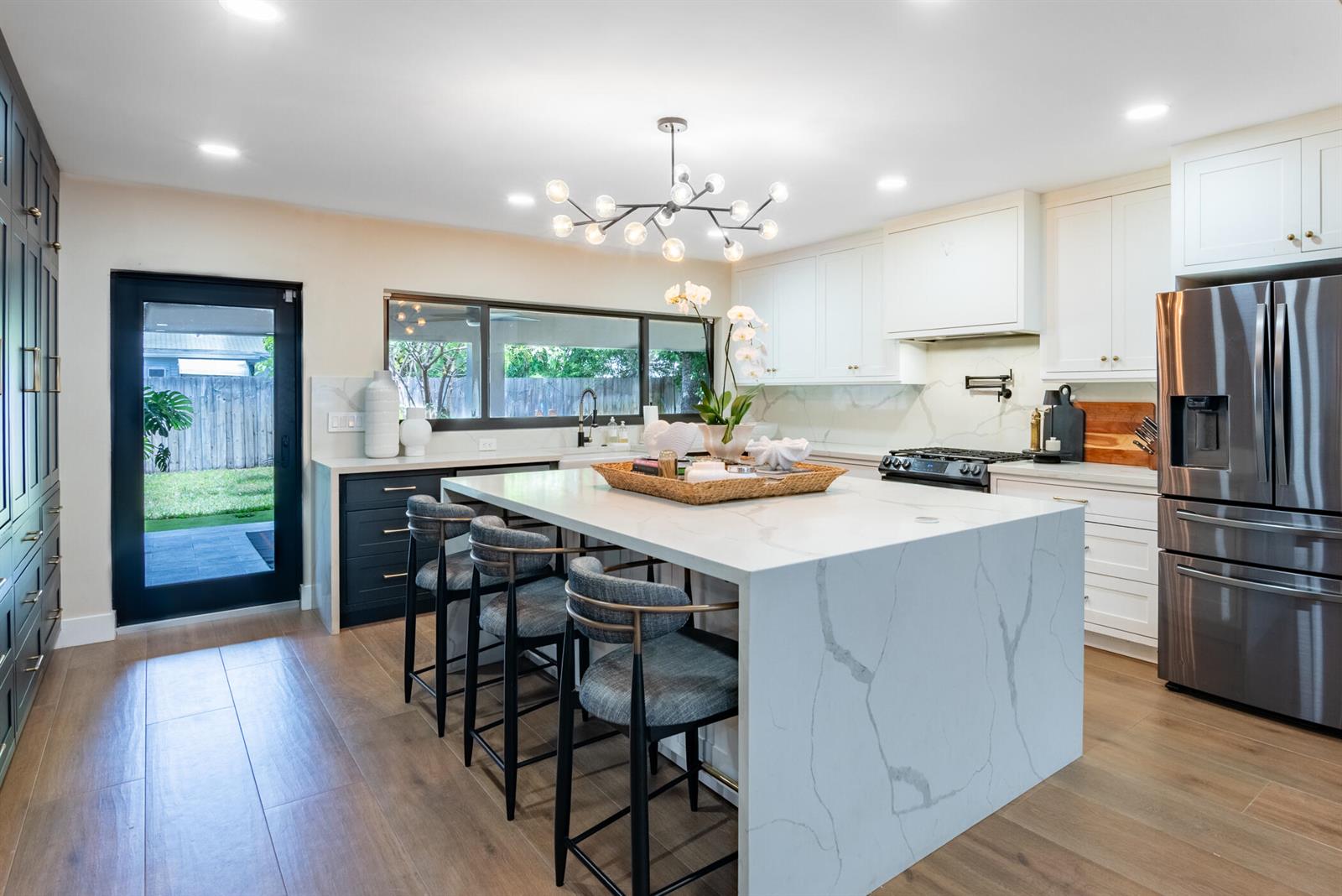 A modern kitchen features a large marble-topped island, white cabinetry, and a black glass door — 335 Franklin Road, West Palm Beach FL 33405, WEST PALM BEACH, FL