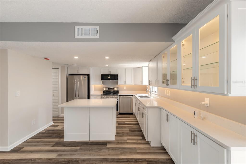 A modern kitchen features white cabinetry, a central island, stainless steel appliances, and wood-look flooring — 625 N HALIFAX AVENUE UNIT 23, DAYTONA BEACH, FL