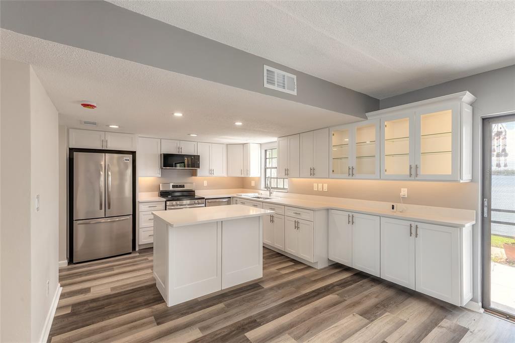 A modern kitchen features white cabinetry, stainless steel appliances, a center island, and wood-look flooring — 625 N HALIFAX AVENUE UNIT 23, DAYTONA BEACH, FL