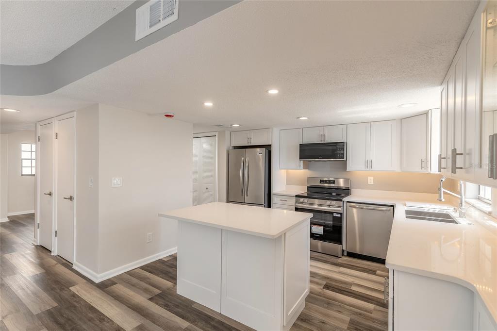 A modern kitchen features white cabinets, stainless steel appliances, a center island, and wood-look flooring — 625 N HALIFAX AVENUE UNIT 23, DAYTONA BEACH, FL