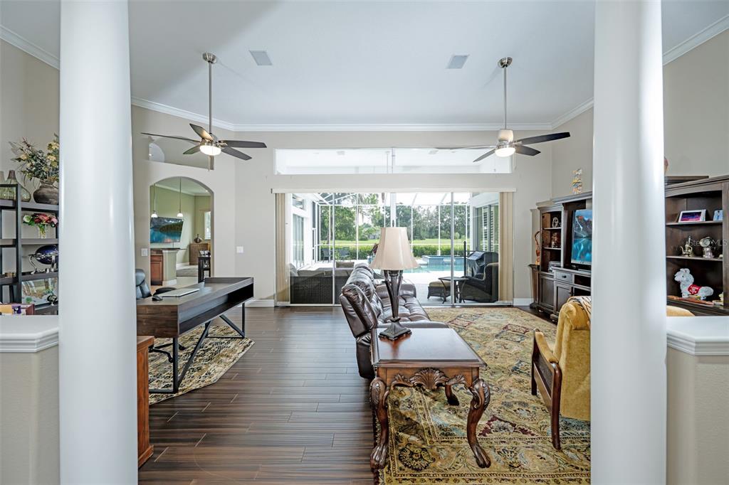 A living room features dark wood flooring, two ceiling fans, and a view of a pool — 5429 BURNT HICKORY DRIVE, VALRICO, FL